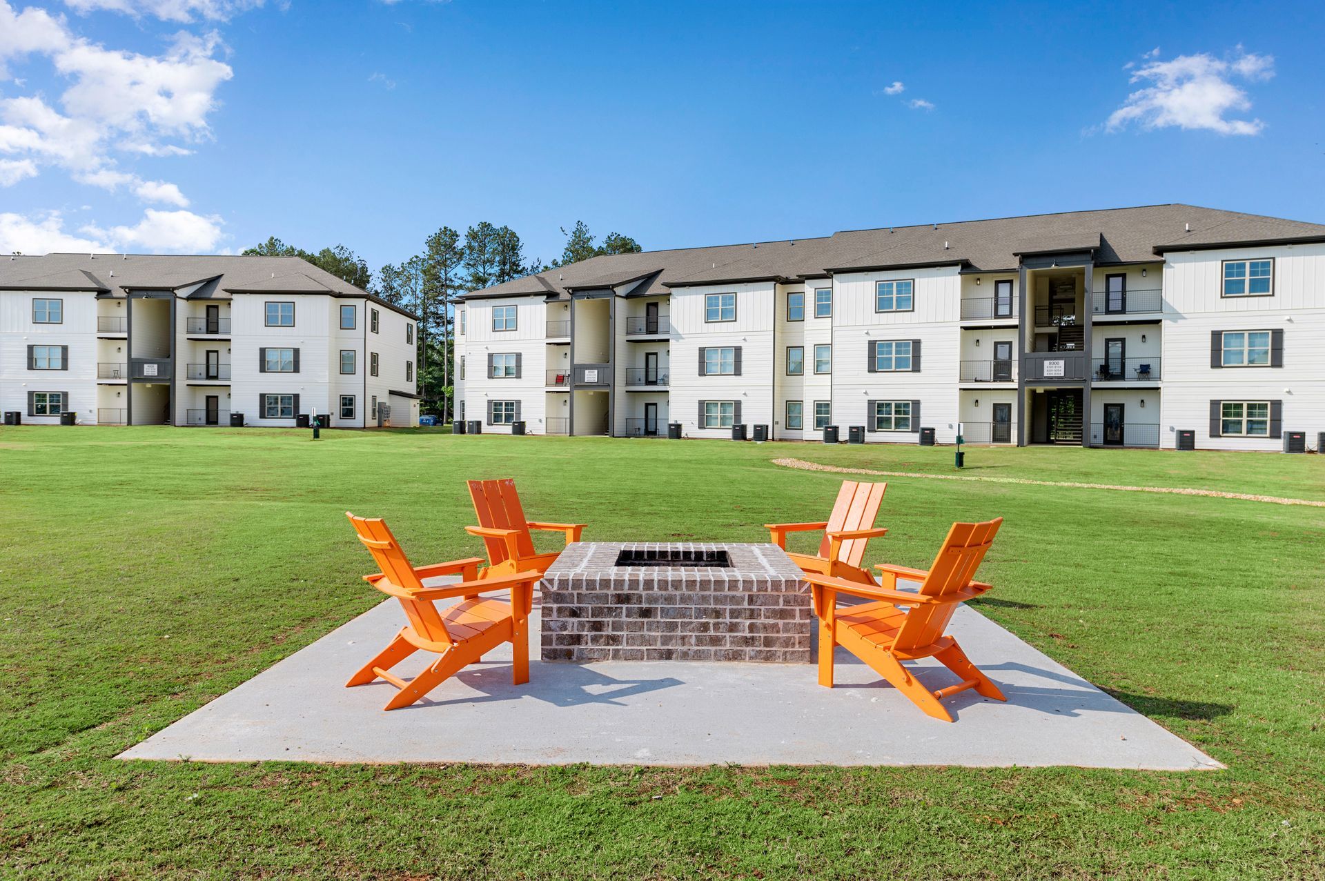 A fire pit with orange chairs in front of the apartment building at Pointe Grand Southlake.