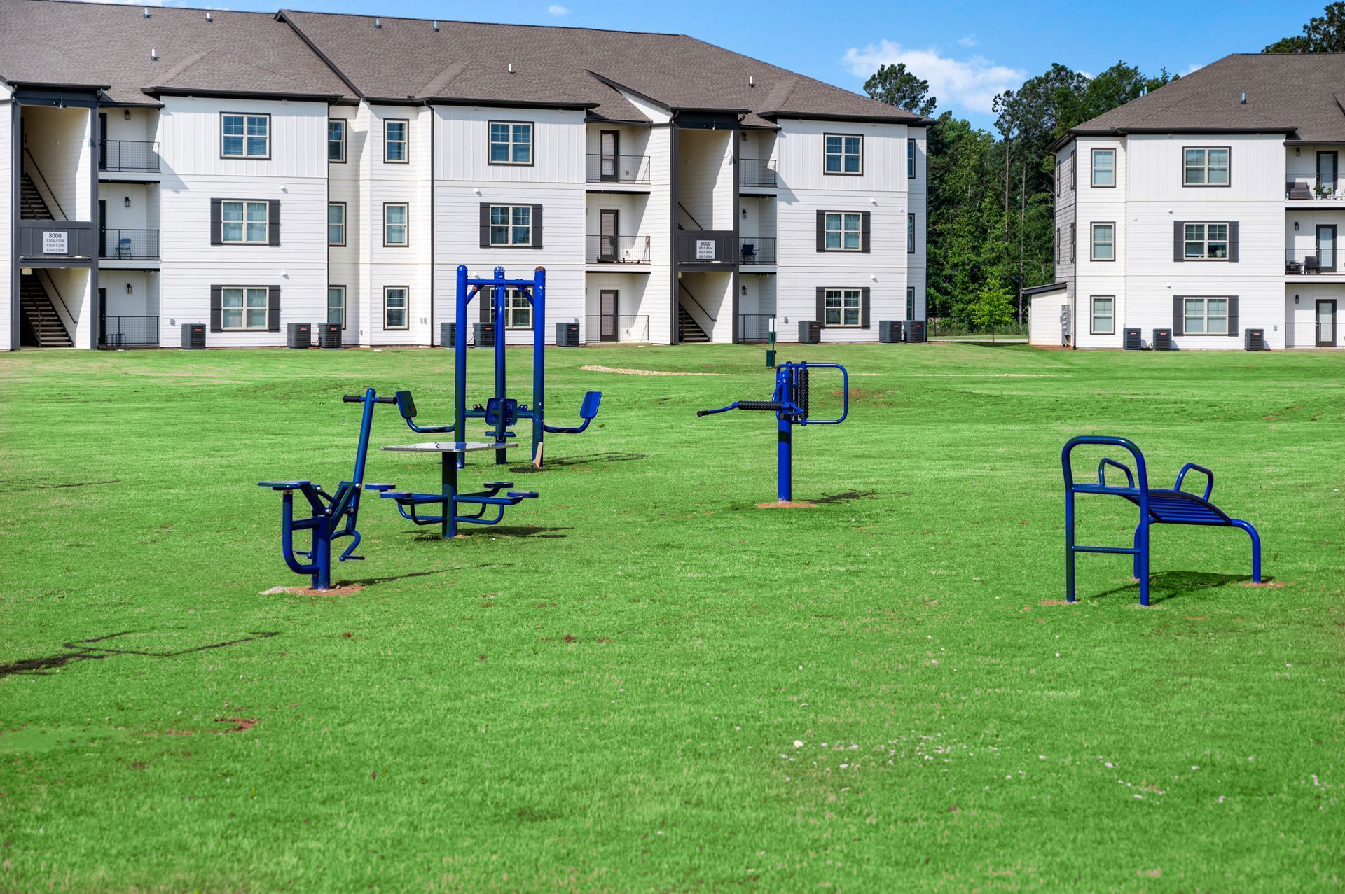 A large grassy field with exercise equipment in front of the apartment building at Pointe Grand Southlake.