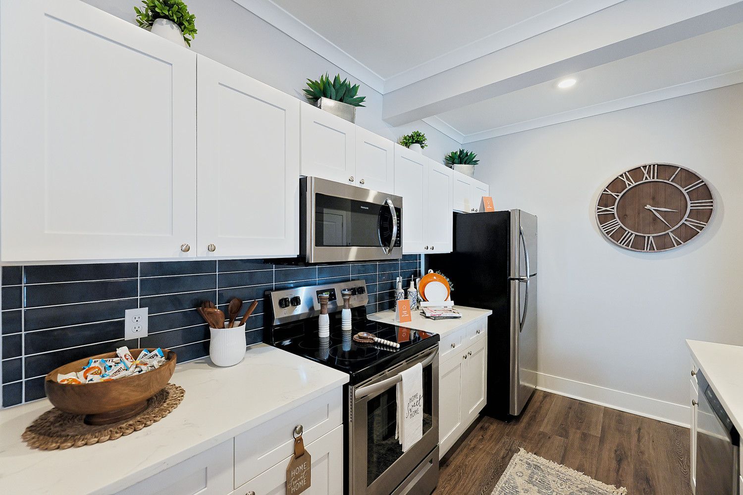 Apartment kitchen with white cabinets, stainless steel appliances, and a clock on the wall.
