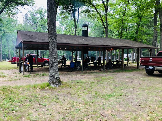 A group of people are sitting under a picnic shelter in the woods.
