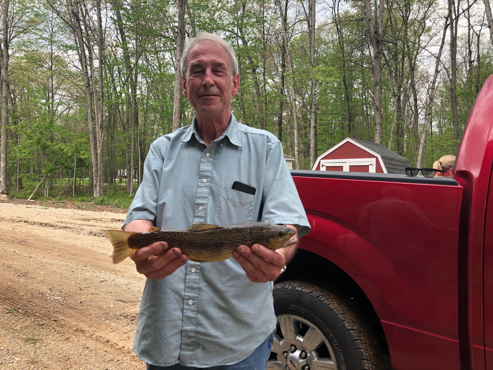 A man is holding a fish in front of a red truck.
