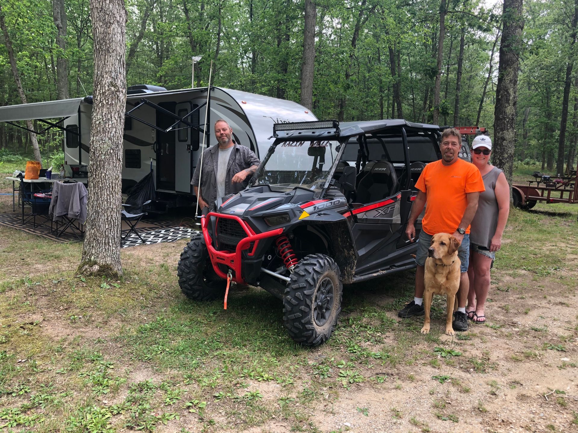 A group of people standing next to a atv and a dog.