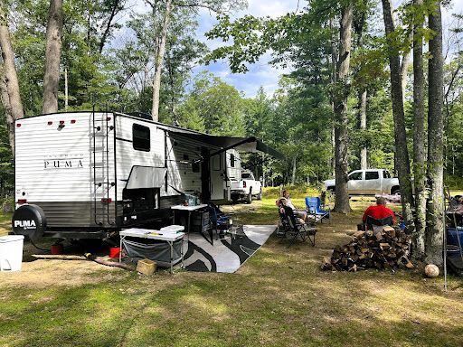 a rv is parked in a campground surrounded by trees .