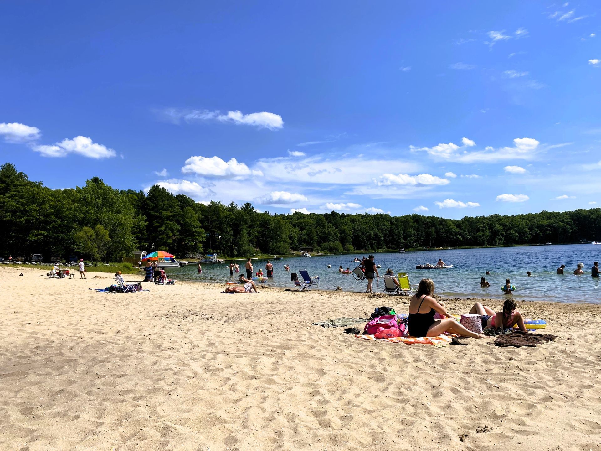 A group of people are sitting on the beach near a lake.