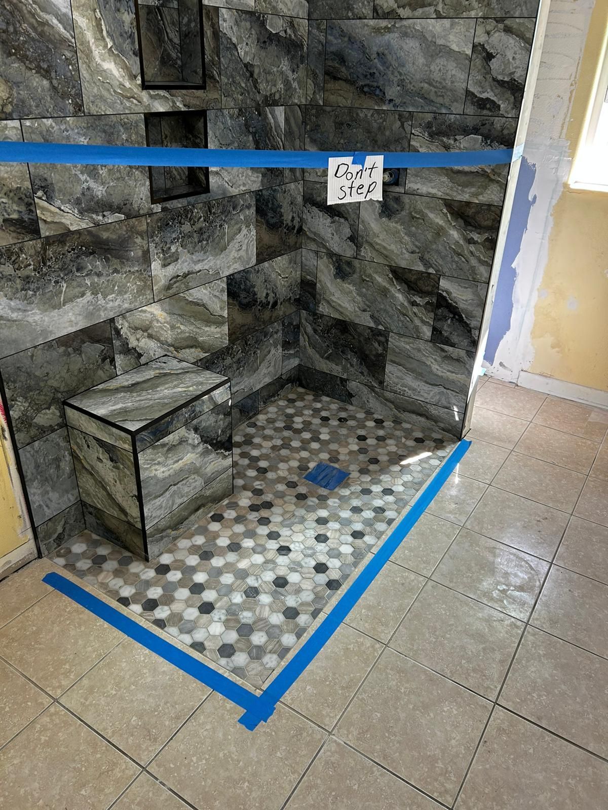 A tiled shower stall with a blue tape around it.