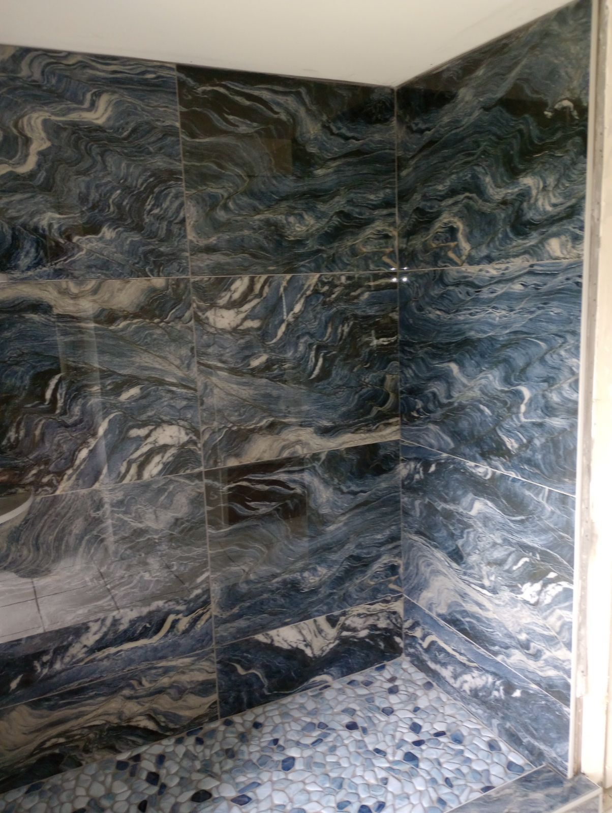 A shower stall with marble tiles and a pebble floor.