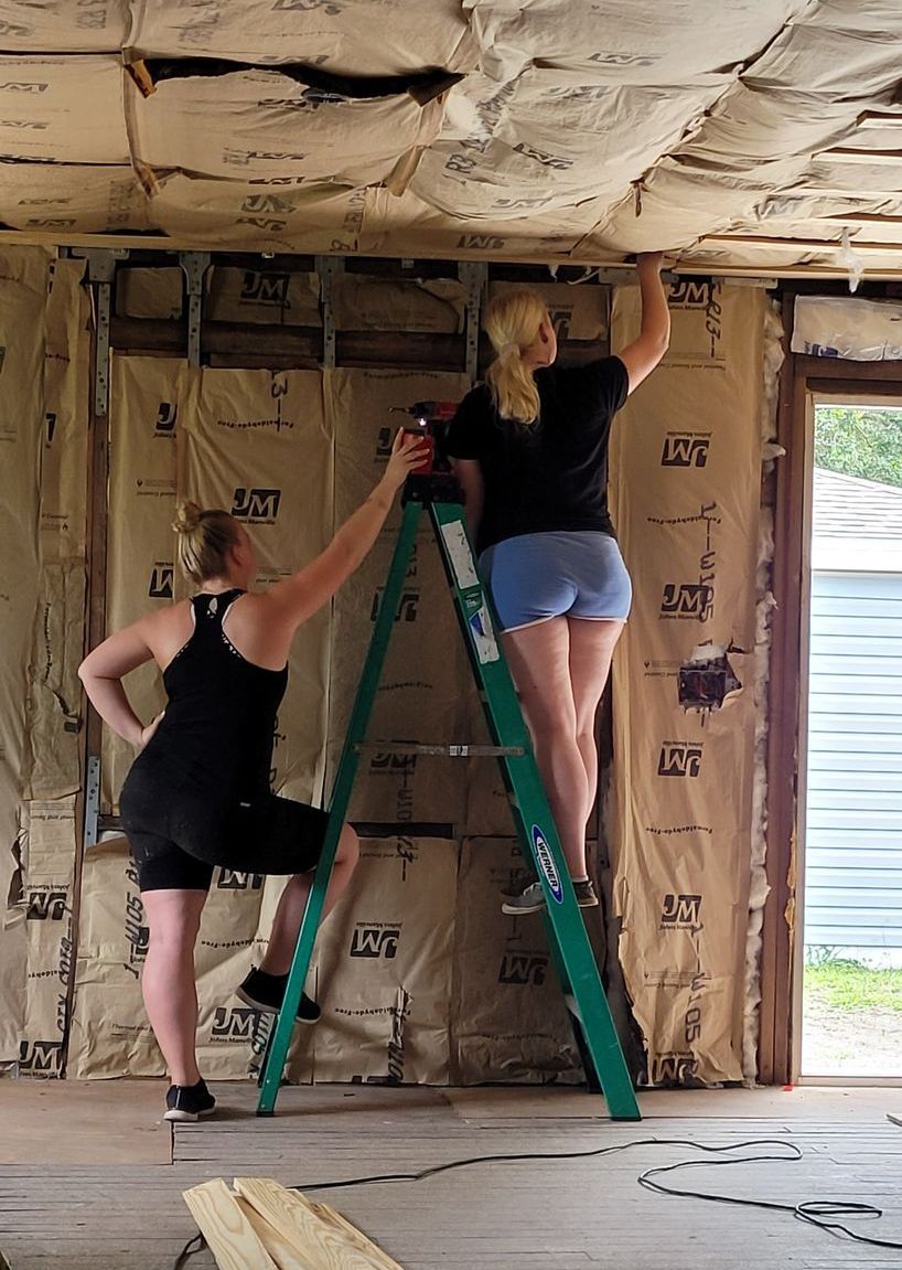 Two women are working on a ladder in a room.