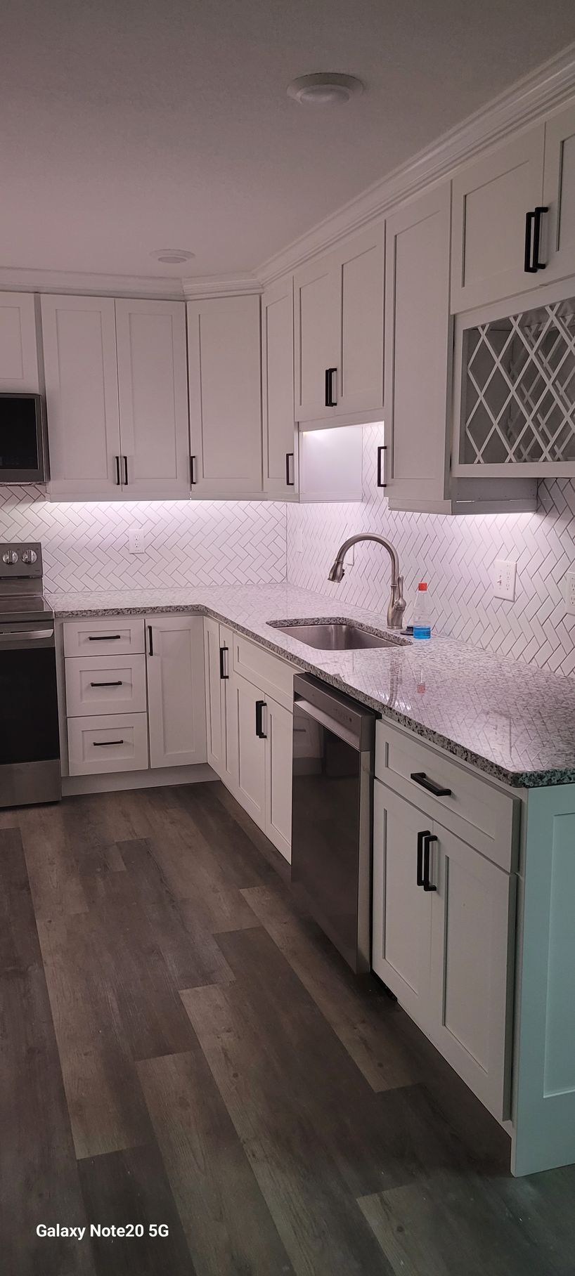 A kitchen with white cabinets , granite counter tops , stainless steel appliances and a sink.