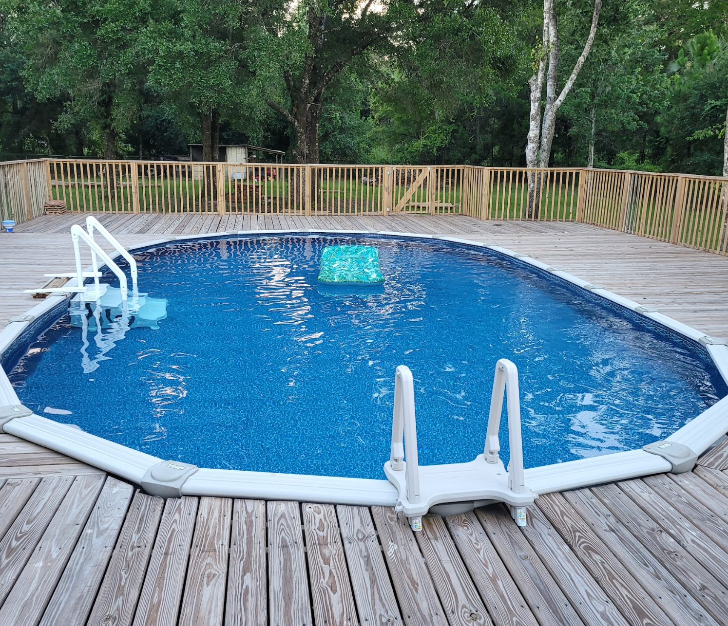 A large swimming pool is surrounded by trees and a wooden deck.