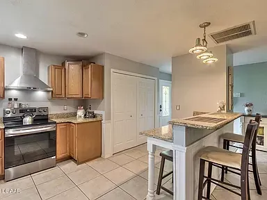 A kitchen with stainless steel appliances , wooden cabinets , granite counter tops and a bar.