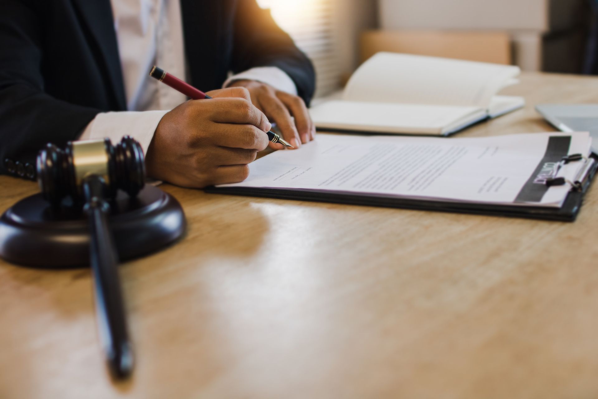 Probate lawyer signing legal documents at office desk with gavel in foreground.
