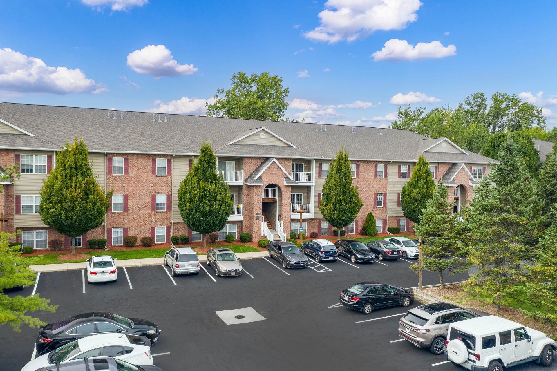 Apartment building with cars parked in front on a sunny day.