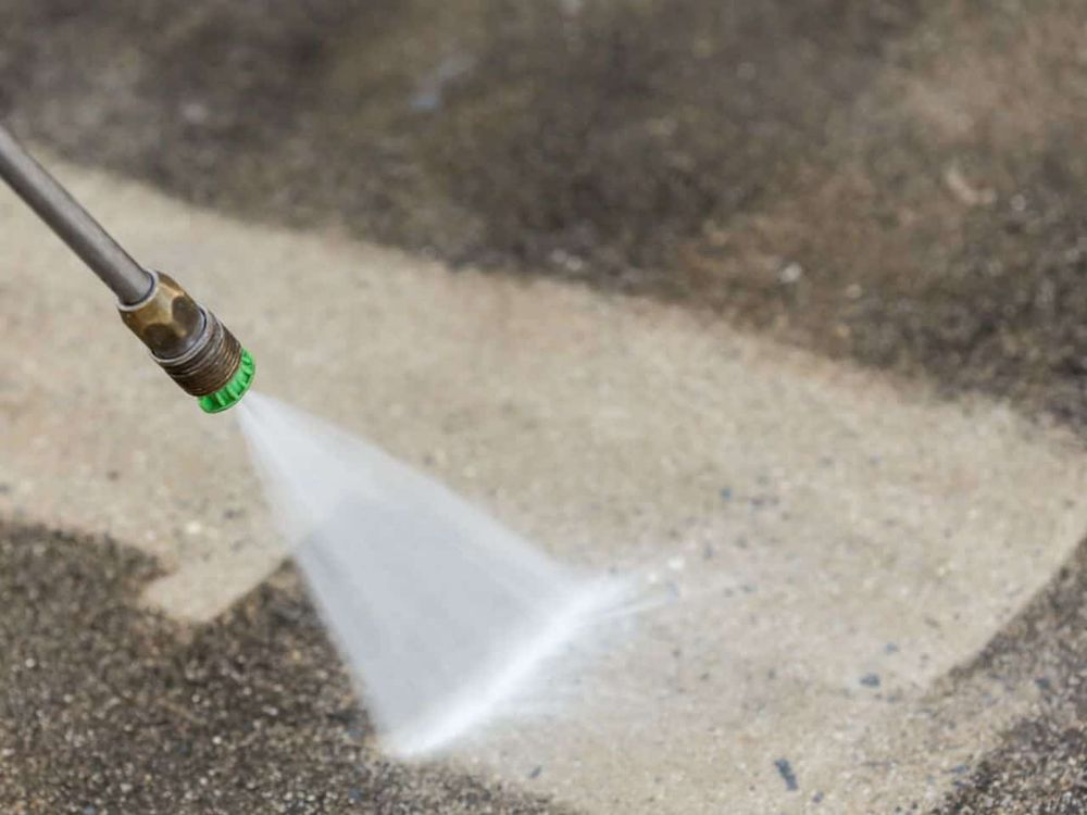 A person is using a high pressure washer to clean a concrete floor.