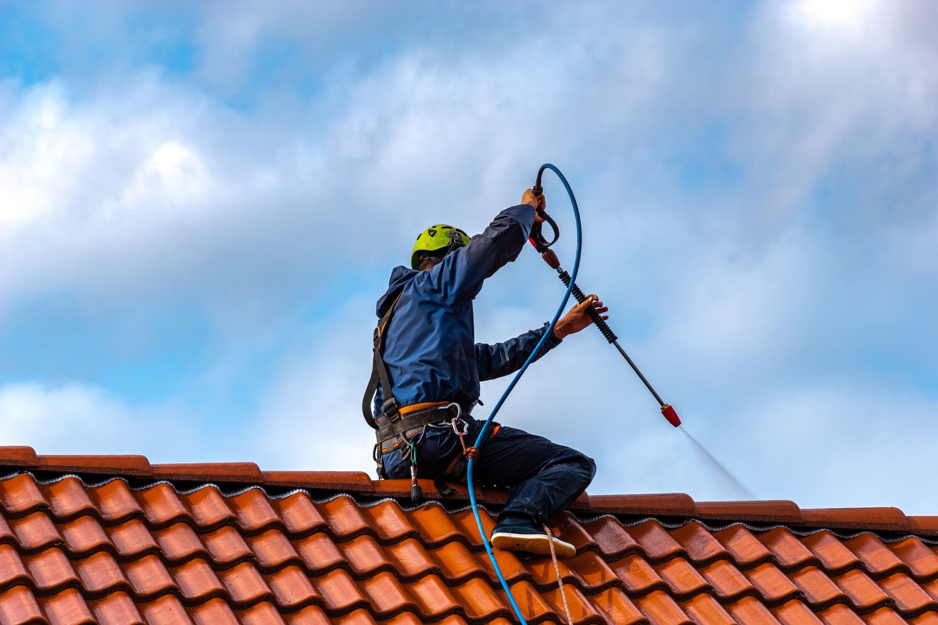 A man is cleaning a tiled roof with a high pressure washer.