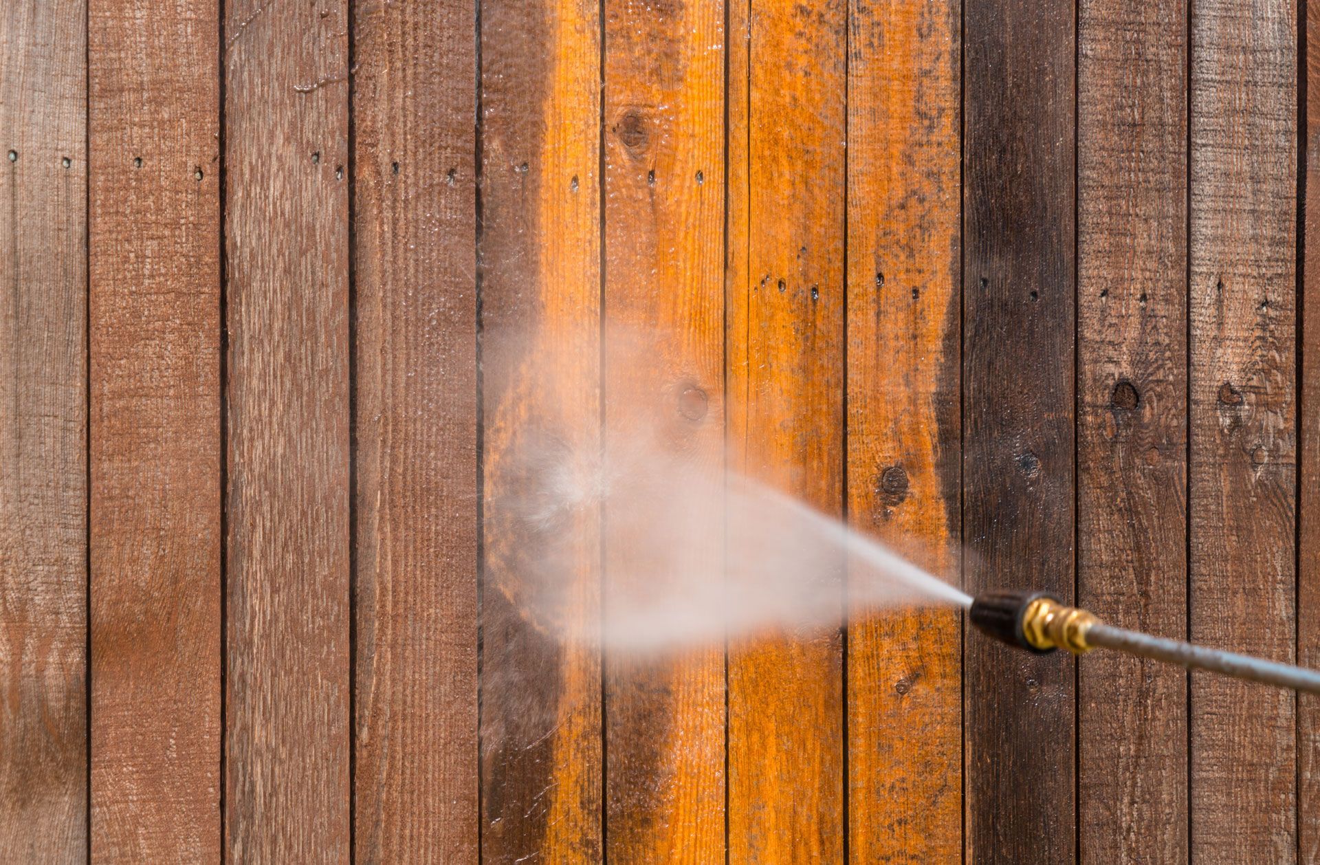 A person is using a high pressure washer to clean a wooden wall.