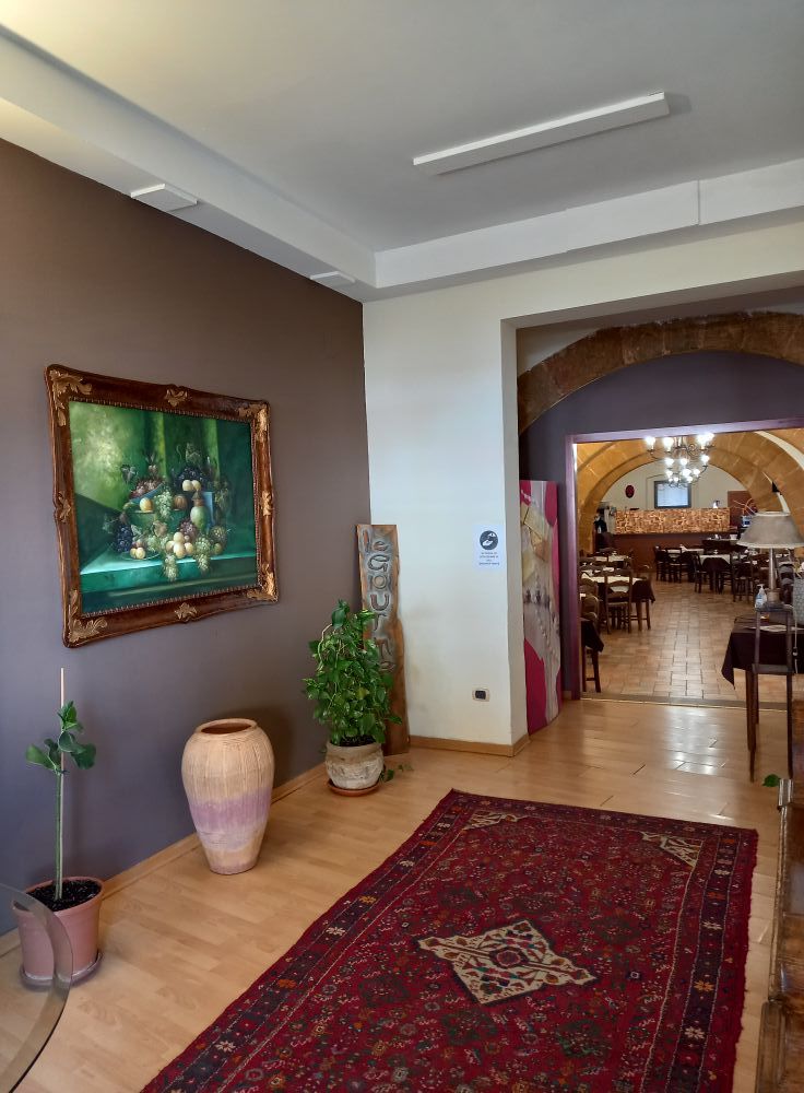 Corridoio con dipinto, tappeto, piante e porta ad arco che conduce alla zona pranzo. Colori rosso scuro, marrone e verde.