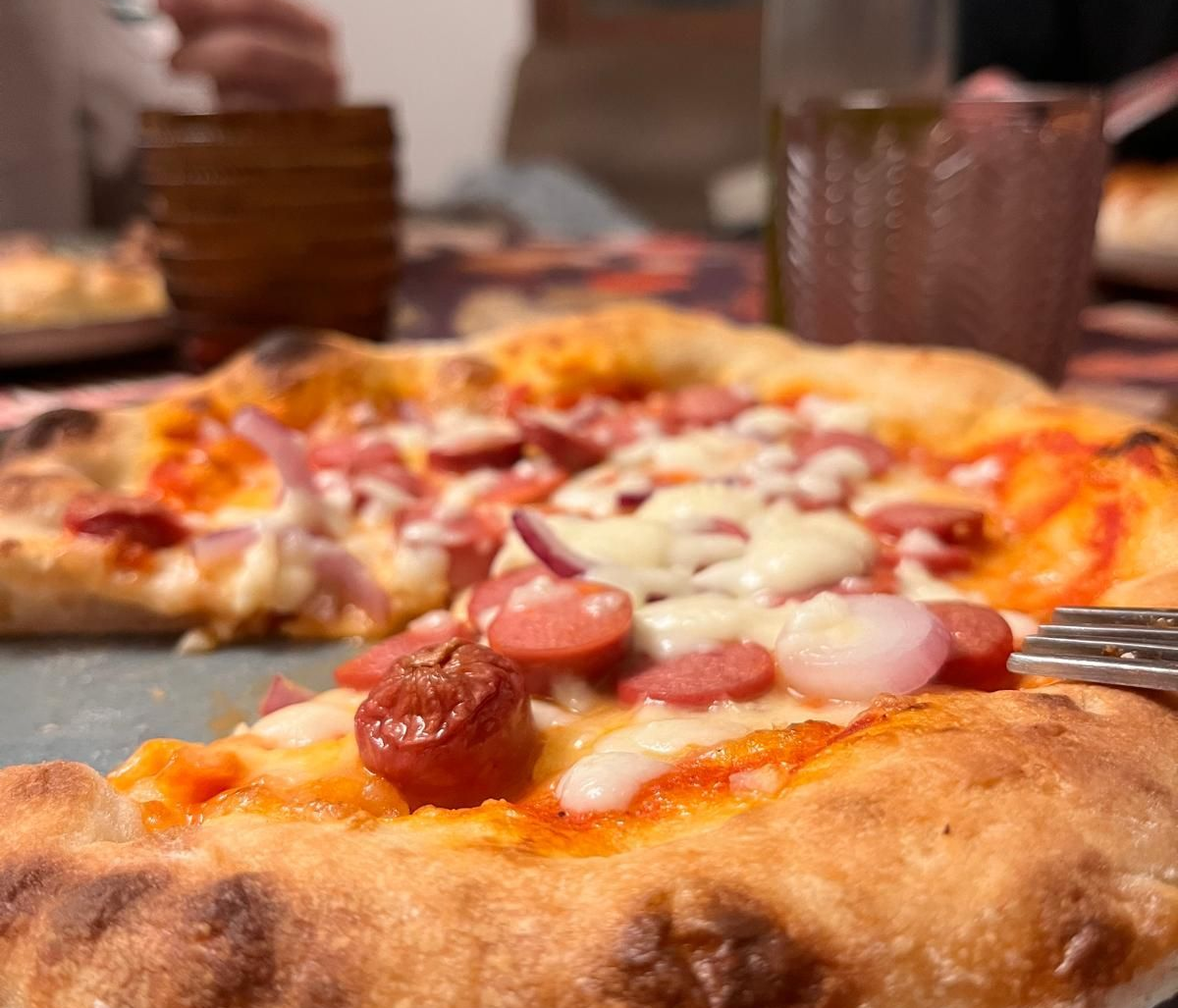 Primo piano di una pizza con salsiccia, cipolle e formaggio; una fetta viene tagliata.