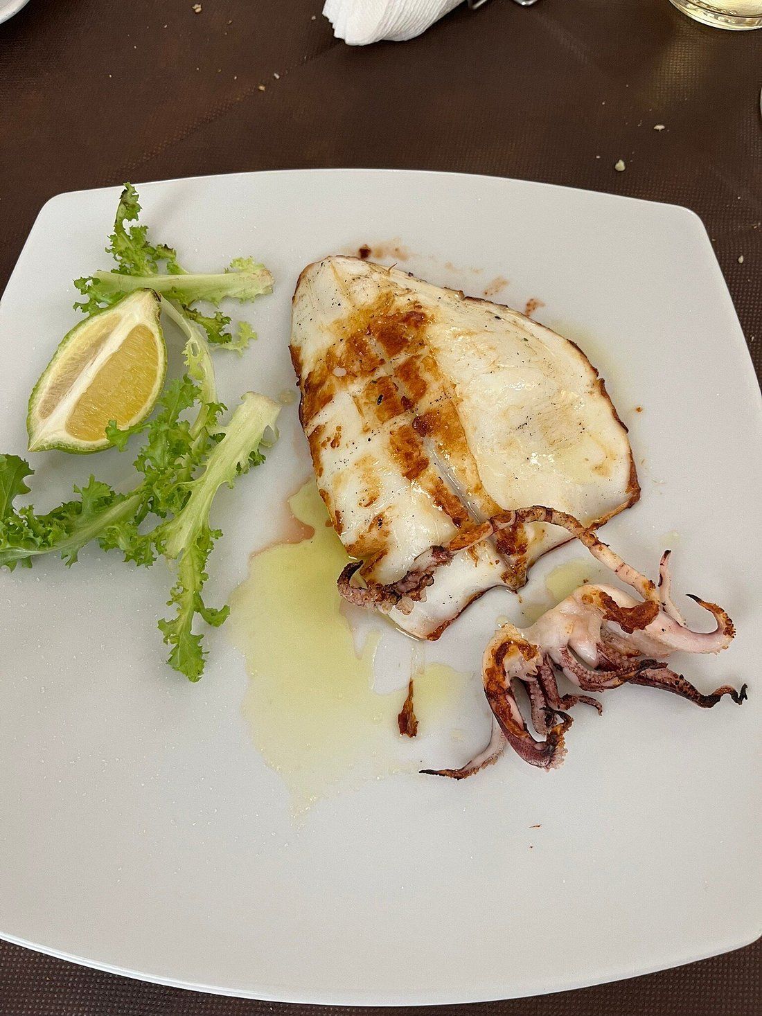 Calamari grigliati con limone e verdure su un piatto bianco.