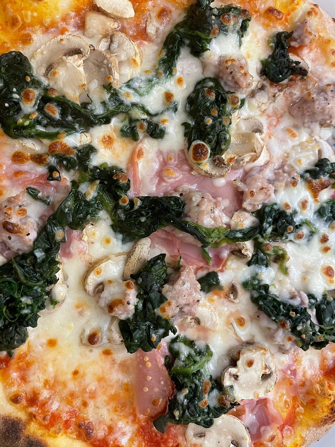 Pizza condita con spinaci, funghi, prosciutto e formaggio.