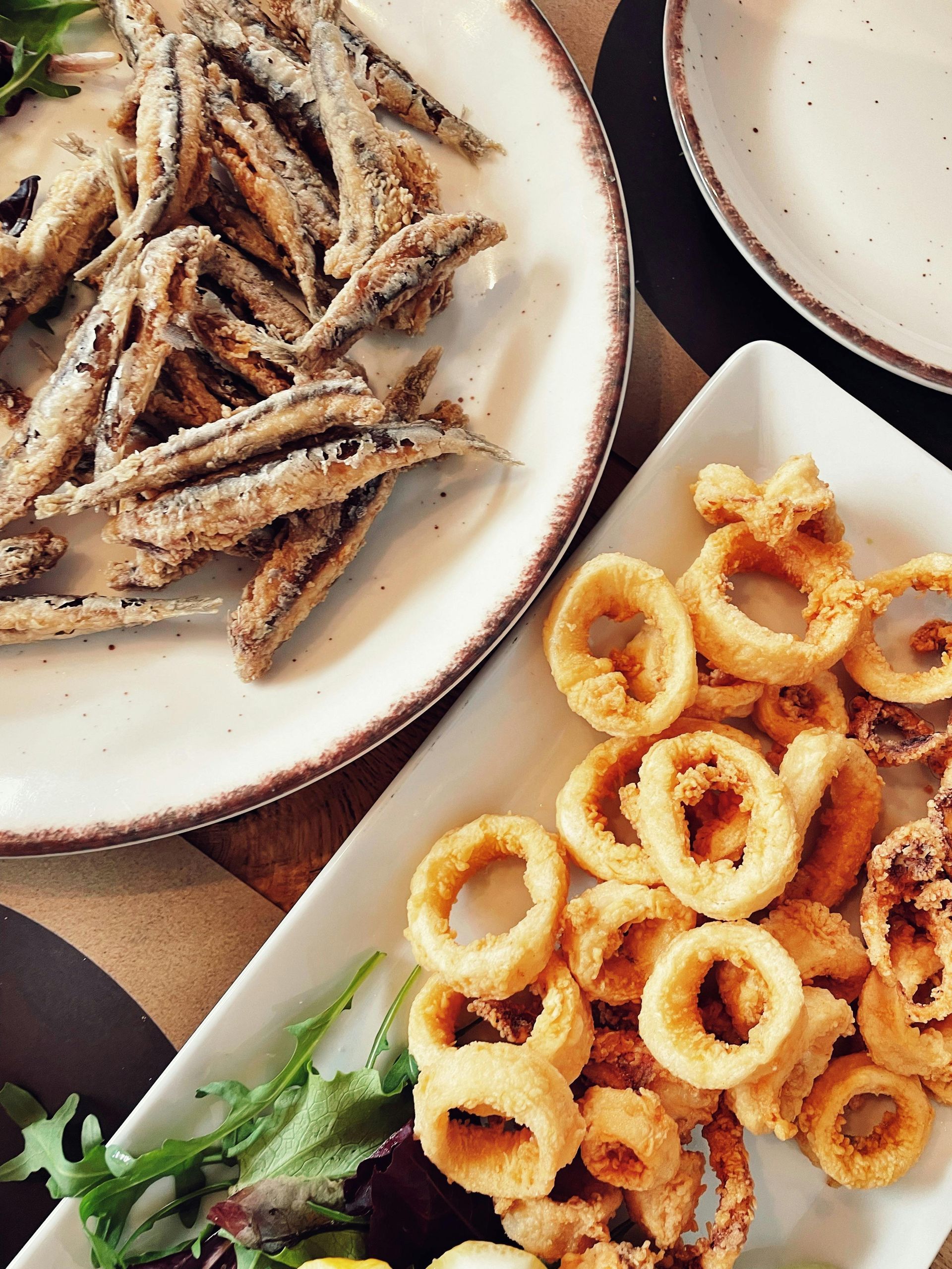 Calamari fritti e pesciolini su piatti bianchi. Primo piano, vista dall'alto.