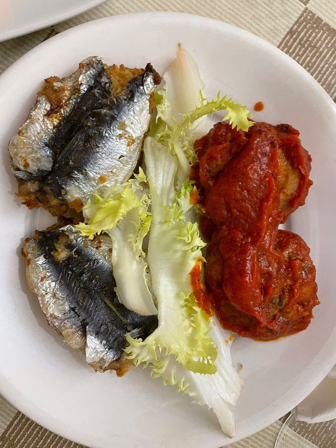 Piatto con sardine fritte, un piatto ricoperto di salsa rossa e lattuga verde arricciata.
