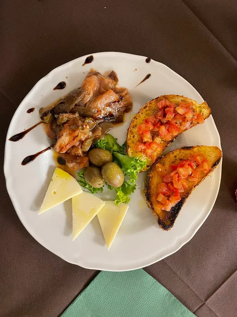 Piatto di antipasti: pane con pomodori, formaggio, olive e un piatto di carne con glassa balsamica.