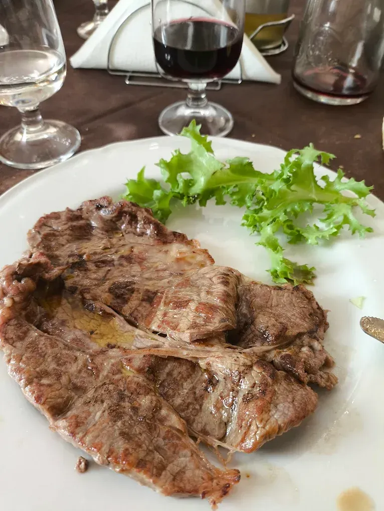 Bistecca su un piatto bianco con lattuga, vino rosso in un bicchiere, ambiente da pranzo.
