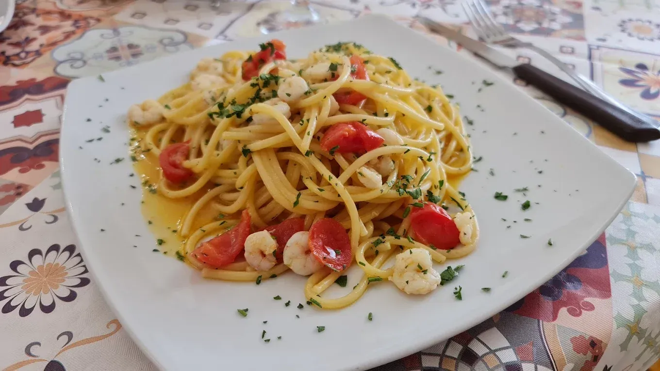 Piatto di spaghetti con pomodori e gamberi su un piatto quadrato bianco, guarnito con prezzemolo.