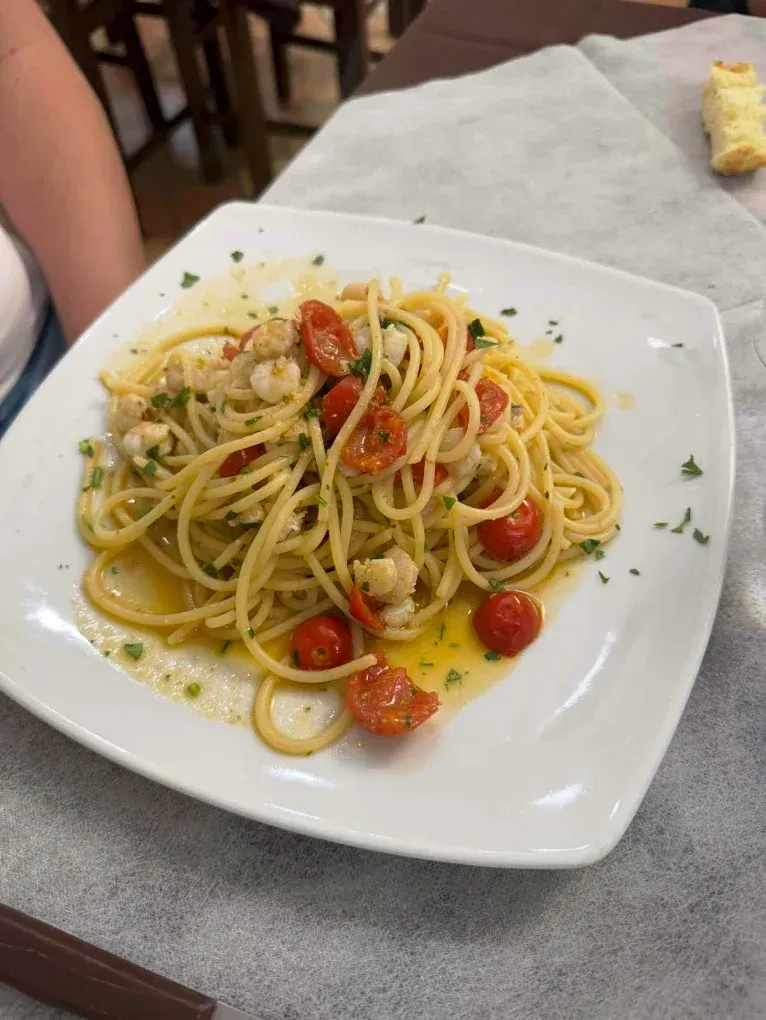 Spaghetti con gamberi e pomodorini su un piatto quadrato bianco, ambientazione ristorante.
