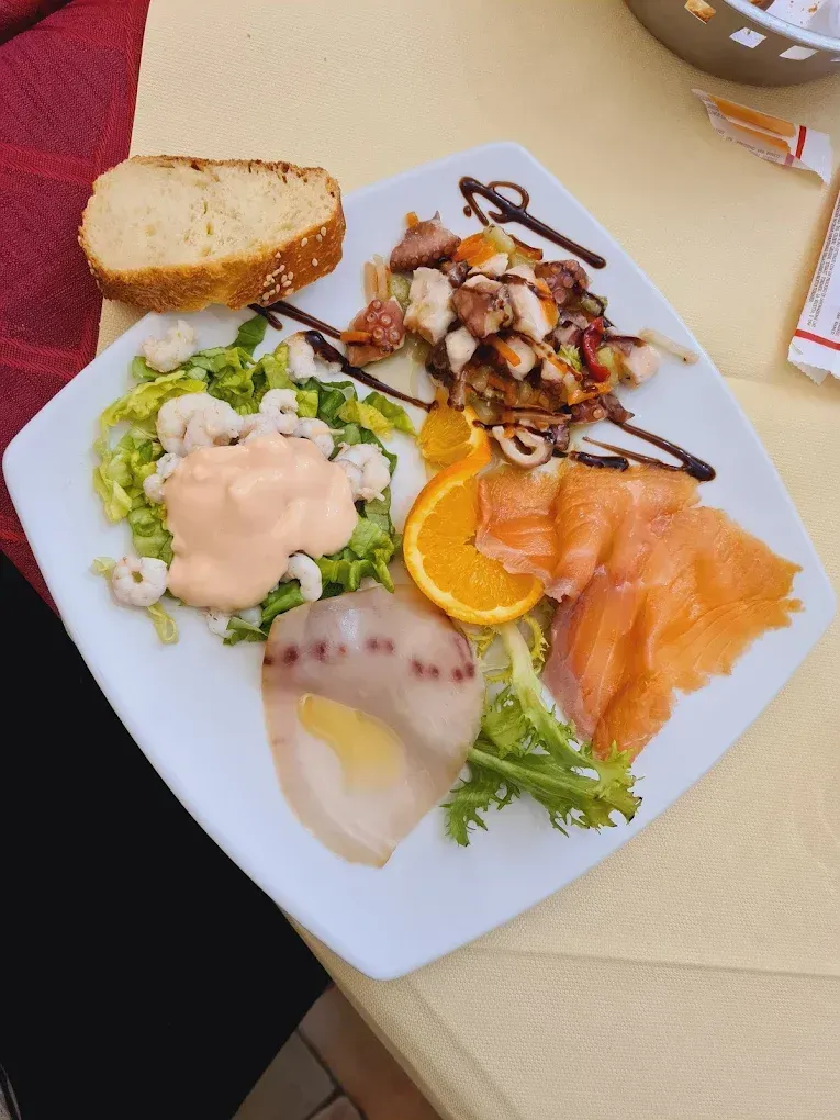 Piatto di antipasti di mare con pane: salmone affumicato, polpo, gamberi e fetta d'arancia.