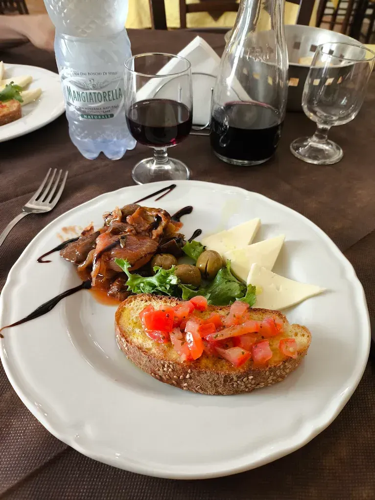 Piatto di cibo: bruschetta, carne, formaggio, olive, vino, acqua e bicchieri su un tavolo.