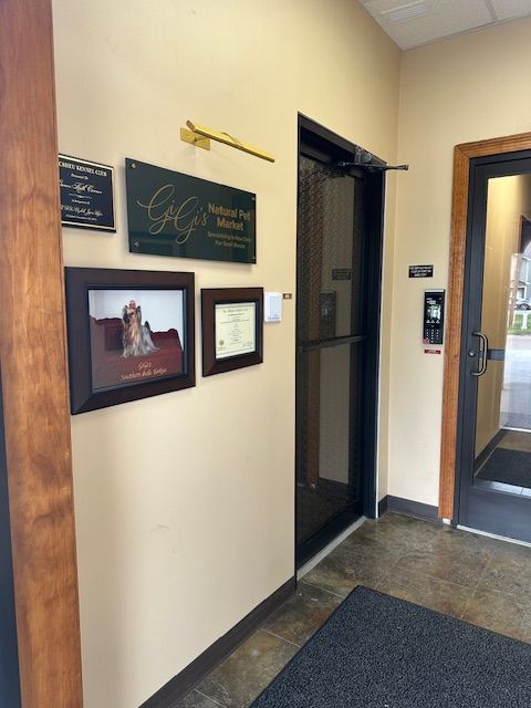 Entrance area with framed art, business sign, elevator, and door. Beige walls, wood trim, dark floor.