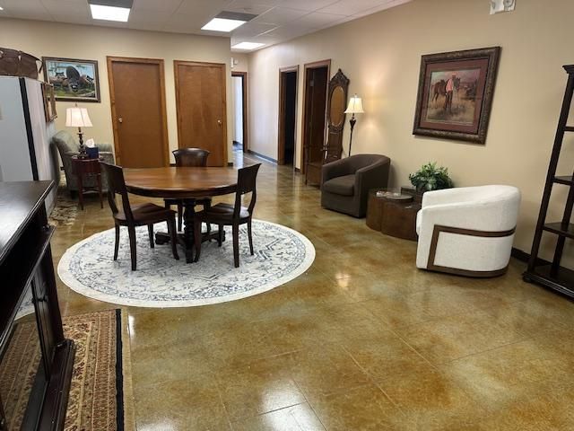 Office interior with round table and chairs on rug, seating area, art on walls, and stained concrete floor.