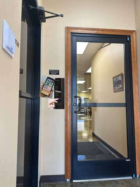 Glass door with access control panel; phone held up to panel. Interior hallway visible.