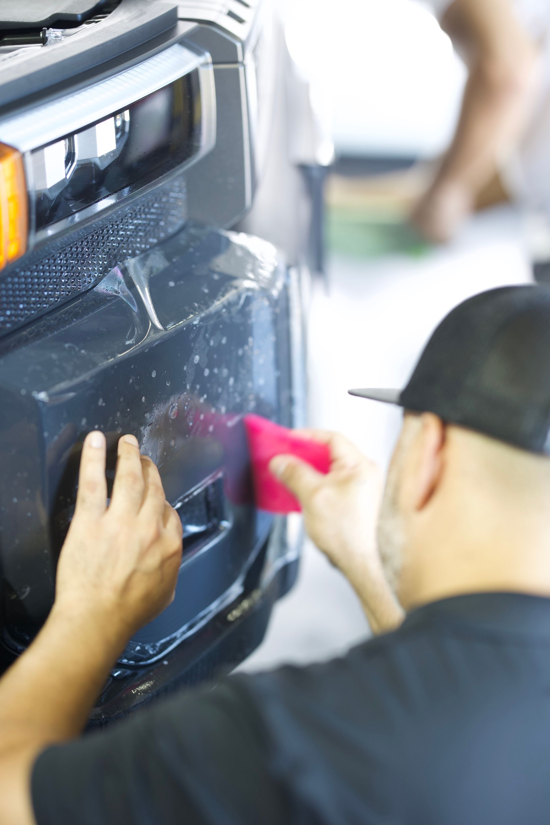 Person applying protective film to a car bumper with a squeegee.