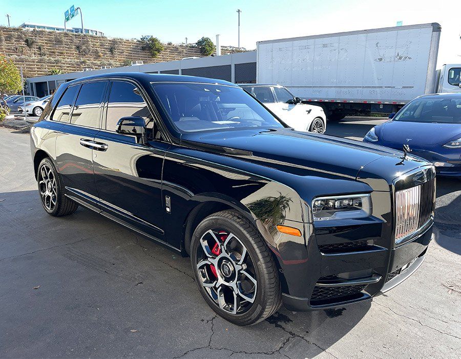 A black rolls royce cullinan is parked in a parking lot next to a white truck.