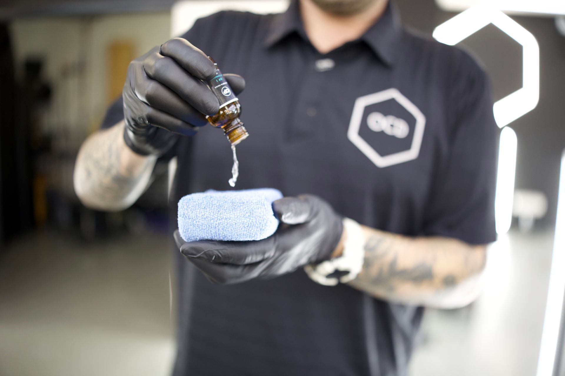 Person in black gloves dripping liquid from a brown bottle onto a red and white object held over a blue cloth.