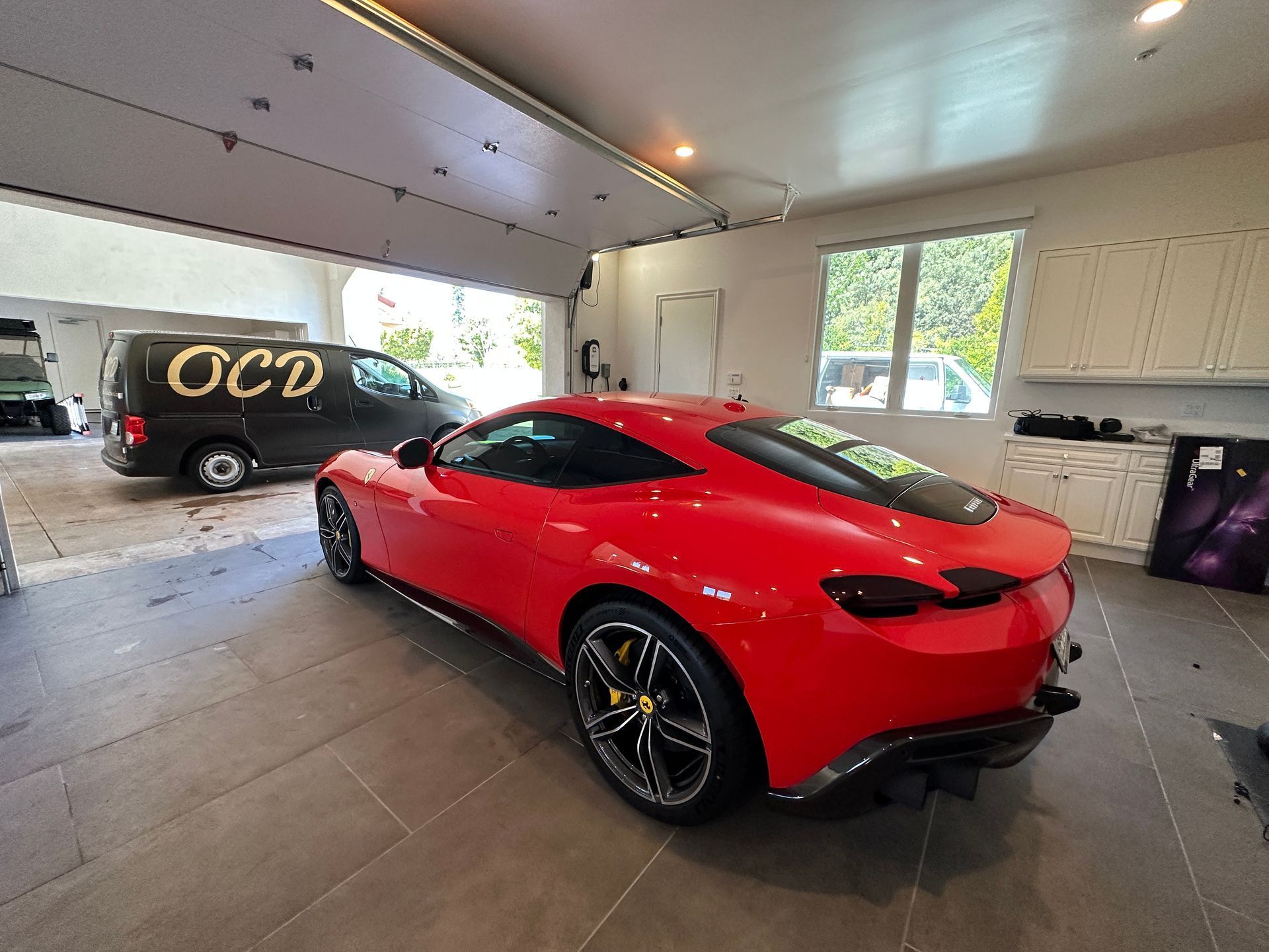 Red Ferrari parked in a garage with the garage door open; a black van is also present.