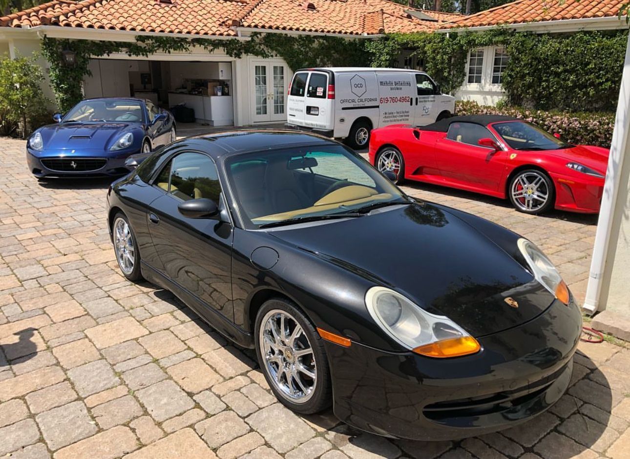 Black Porsche in front of a blue and red sports car parked on a brick driveway.