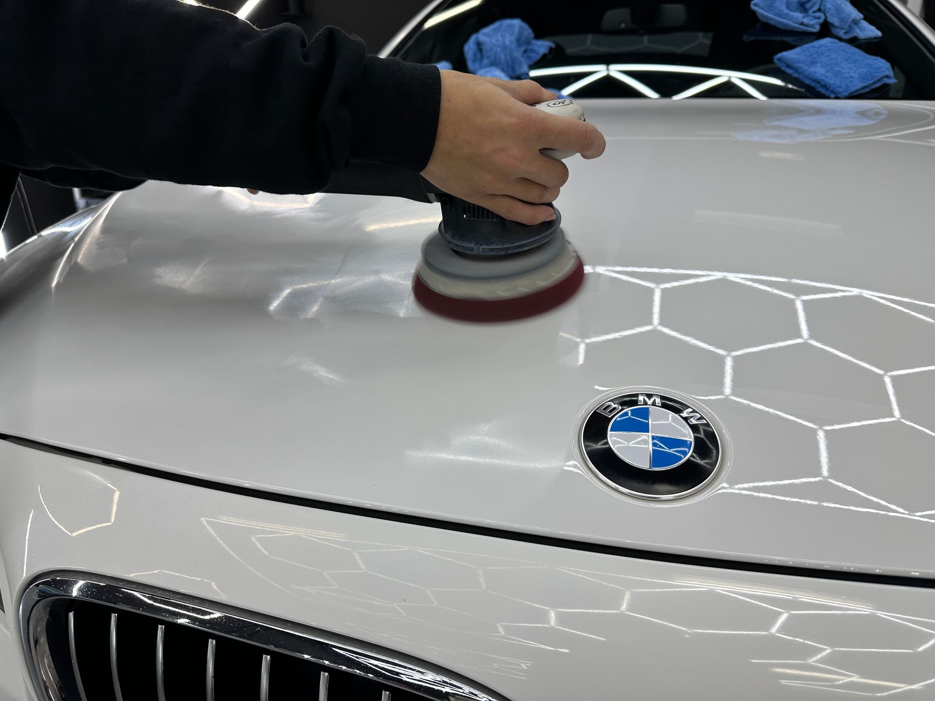 A person is polishing the hood of a white bmw
