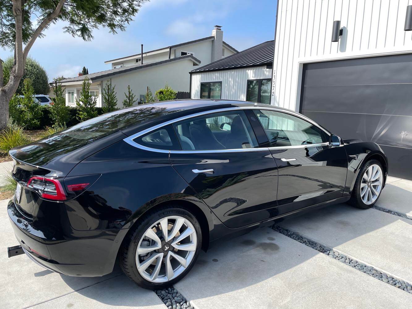 A black tesla model 3 is parked in front of a garage.