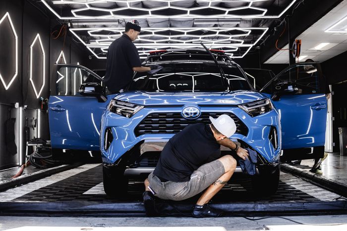Two people detailing a blue SUV in a well-lit car wash bay.