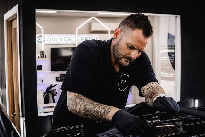 Man wearing black gloves and shirt cleaning a car interior in a shop.