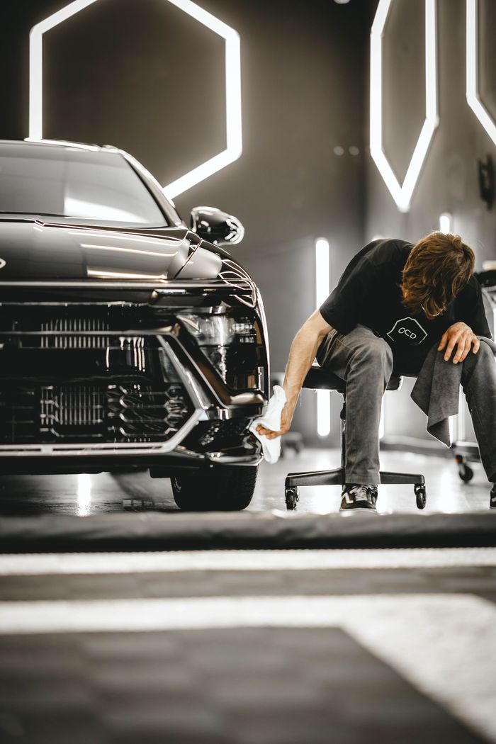 A person cleaning the front bumper of a black car with a white cloth inside a detail shop.