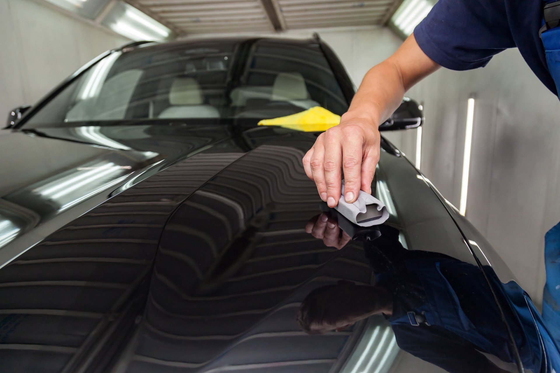 A man is polishing the hood of a black car.