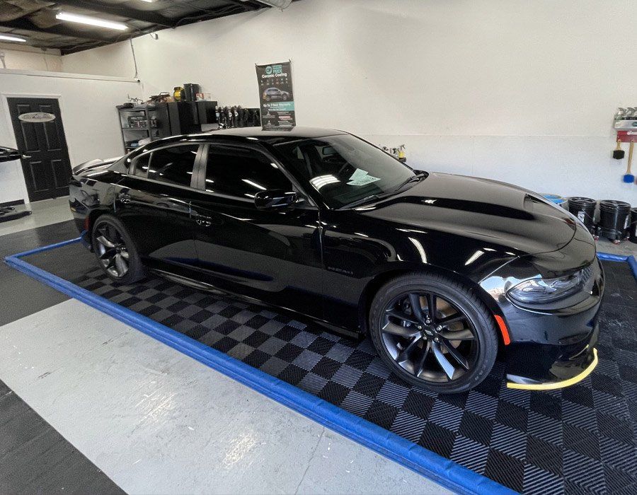 A black dodge charger is parked on a checkered mat in a garage.