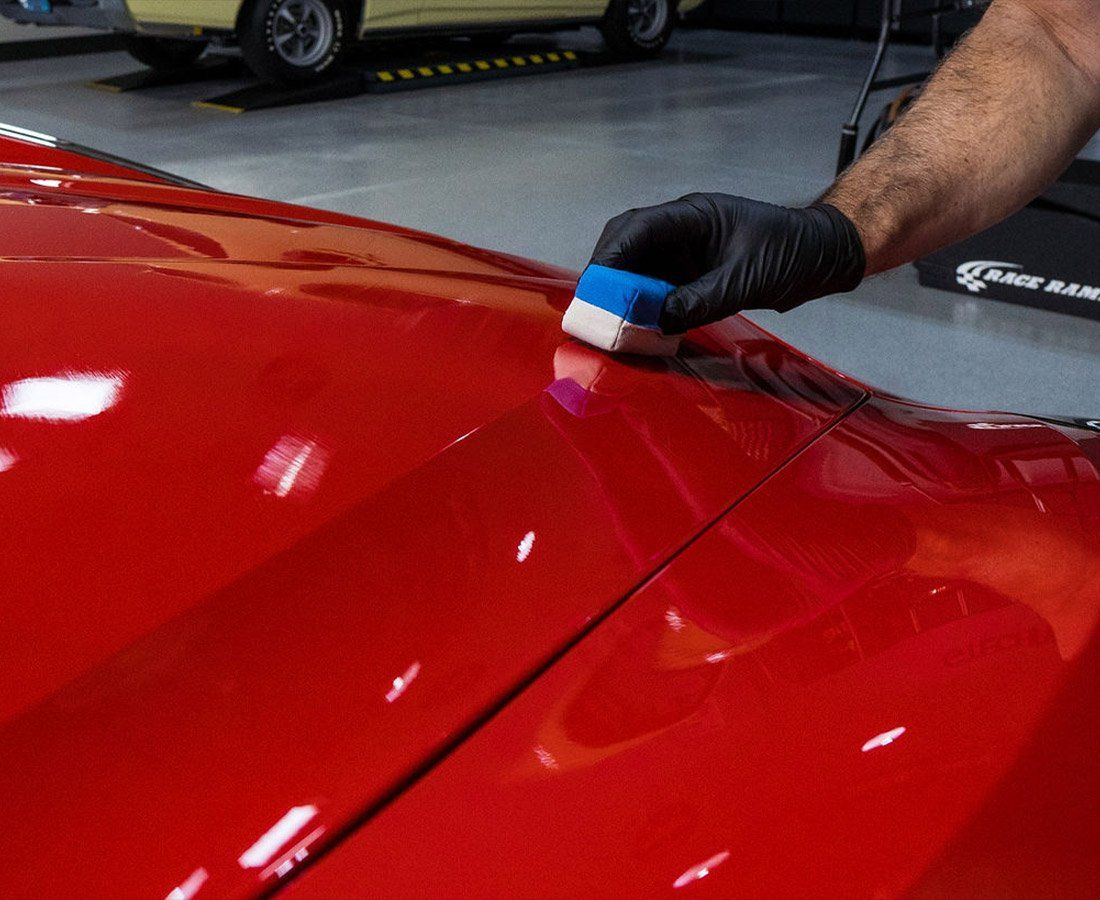 A person is polishing the hood of a red car.