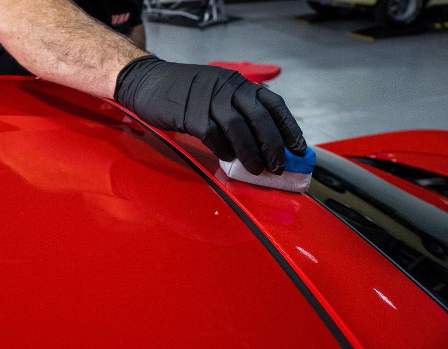 A person is polishing a red car with a sponge.