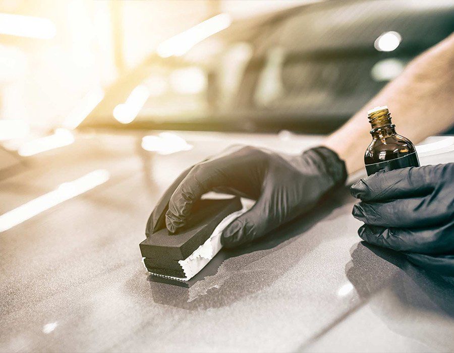 A person wearing black gloves is polishing the hood of a car.