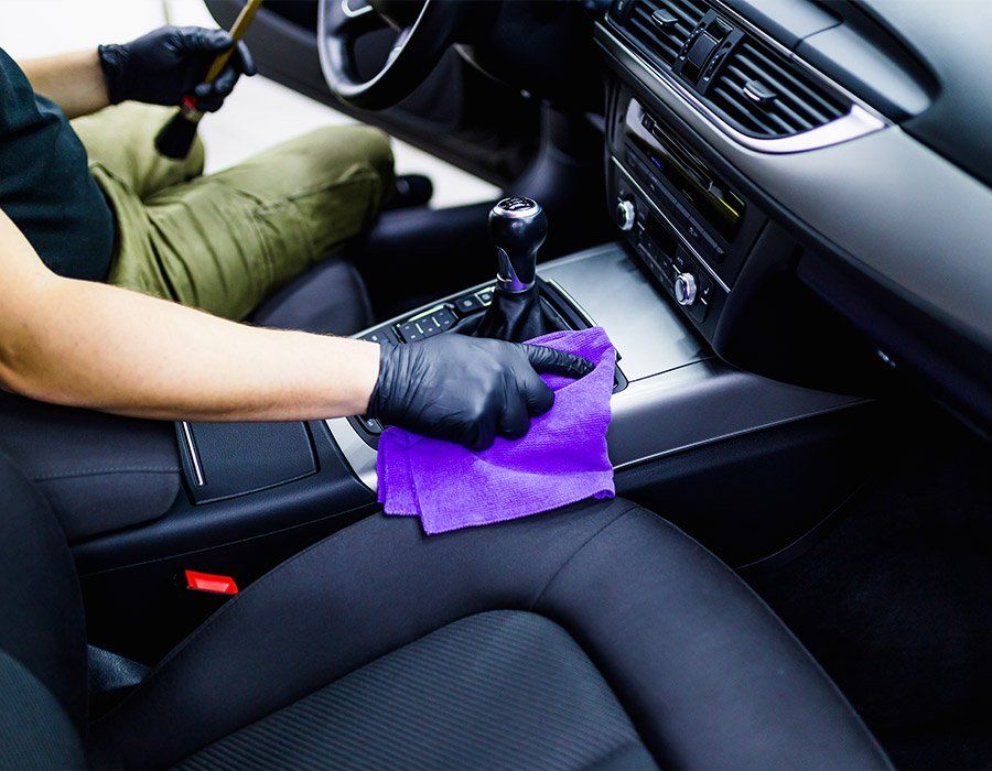 A person is cleaning the interior of a car with a purple cloth.
